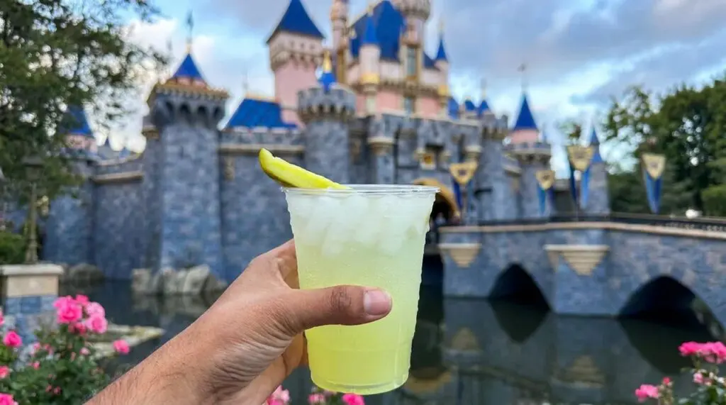 Sparkling Pickle Lemonade at the Disneyland Resort holding the cup in front of Sleeping Beauty's Castle