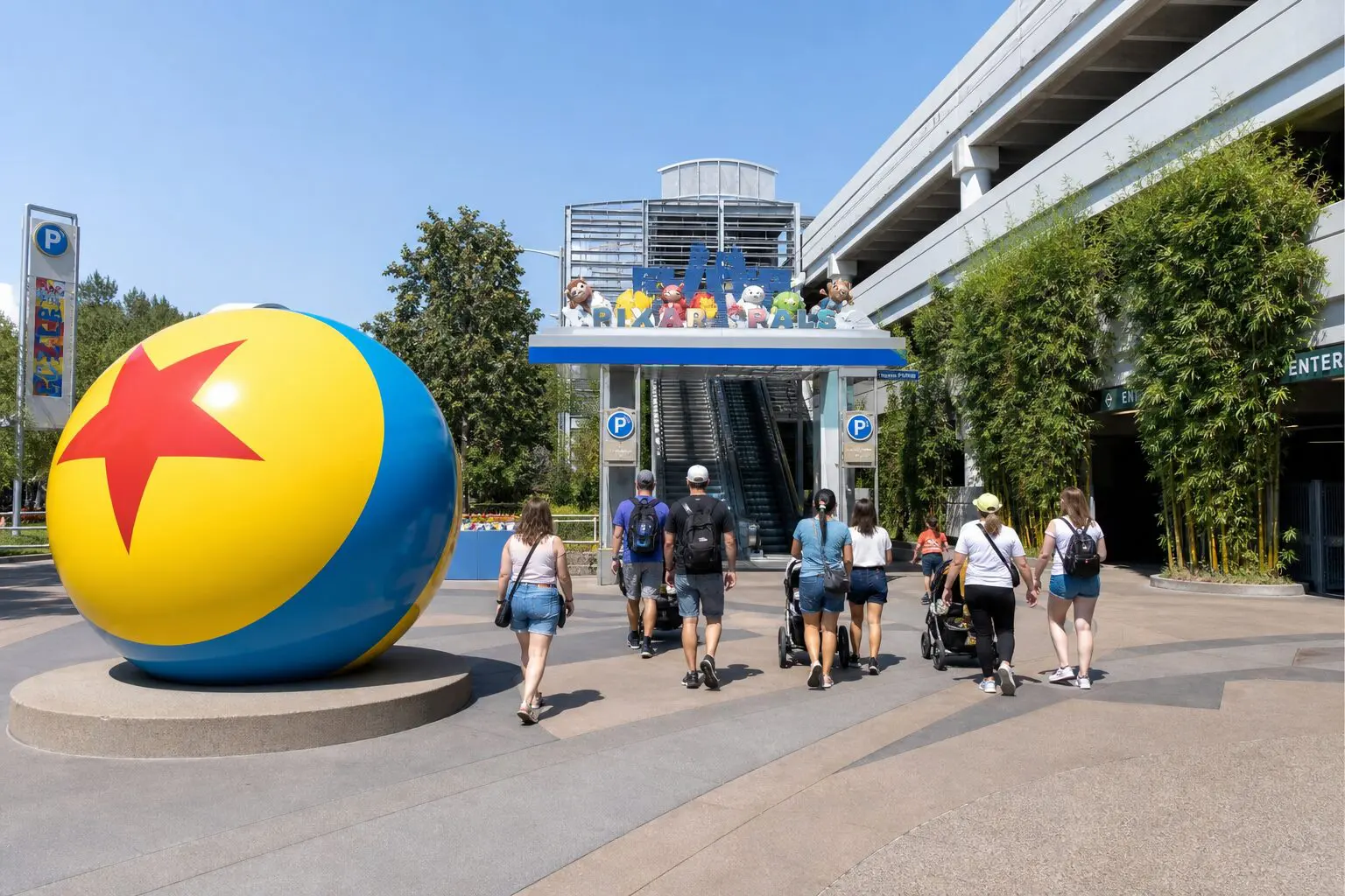 Pixar Pals parking structure plaza at Disneyland on a bright morning, with the yellow Pixar ball in the foreground and guests walking toward the garage escalators