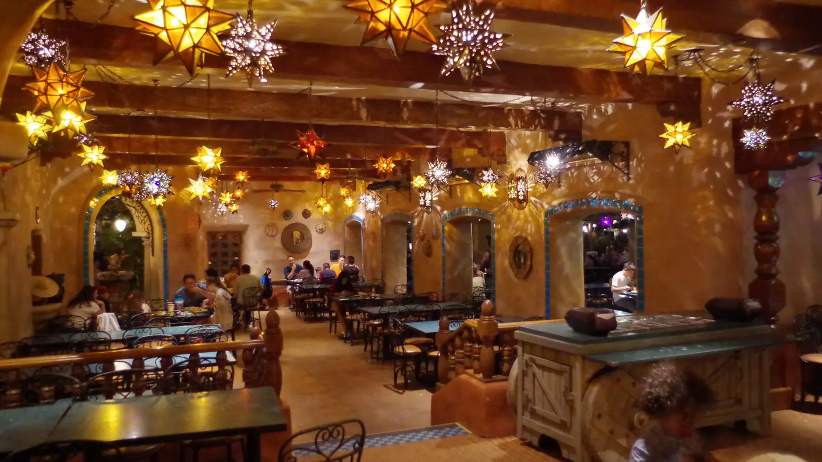 Indoor dining room at Rancho del Zocalo Restaurante at Disneyland with star shaped lanterns hanging from wood beams and guests seated at tables